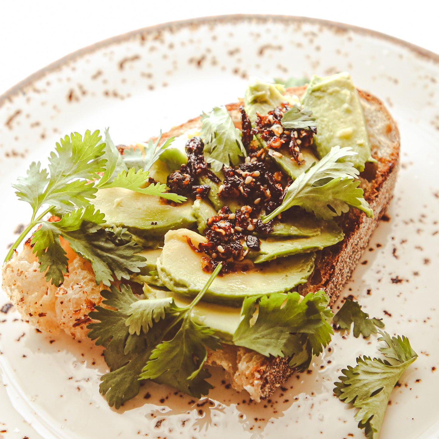 Toast with avocado slices, cilantro, and chile sauce on small plate.