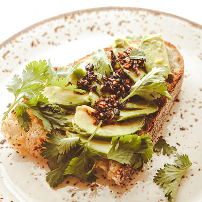 Toast with avocado slices, cilantro, and chile sauce on small plate.