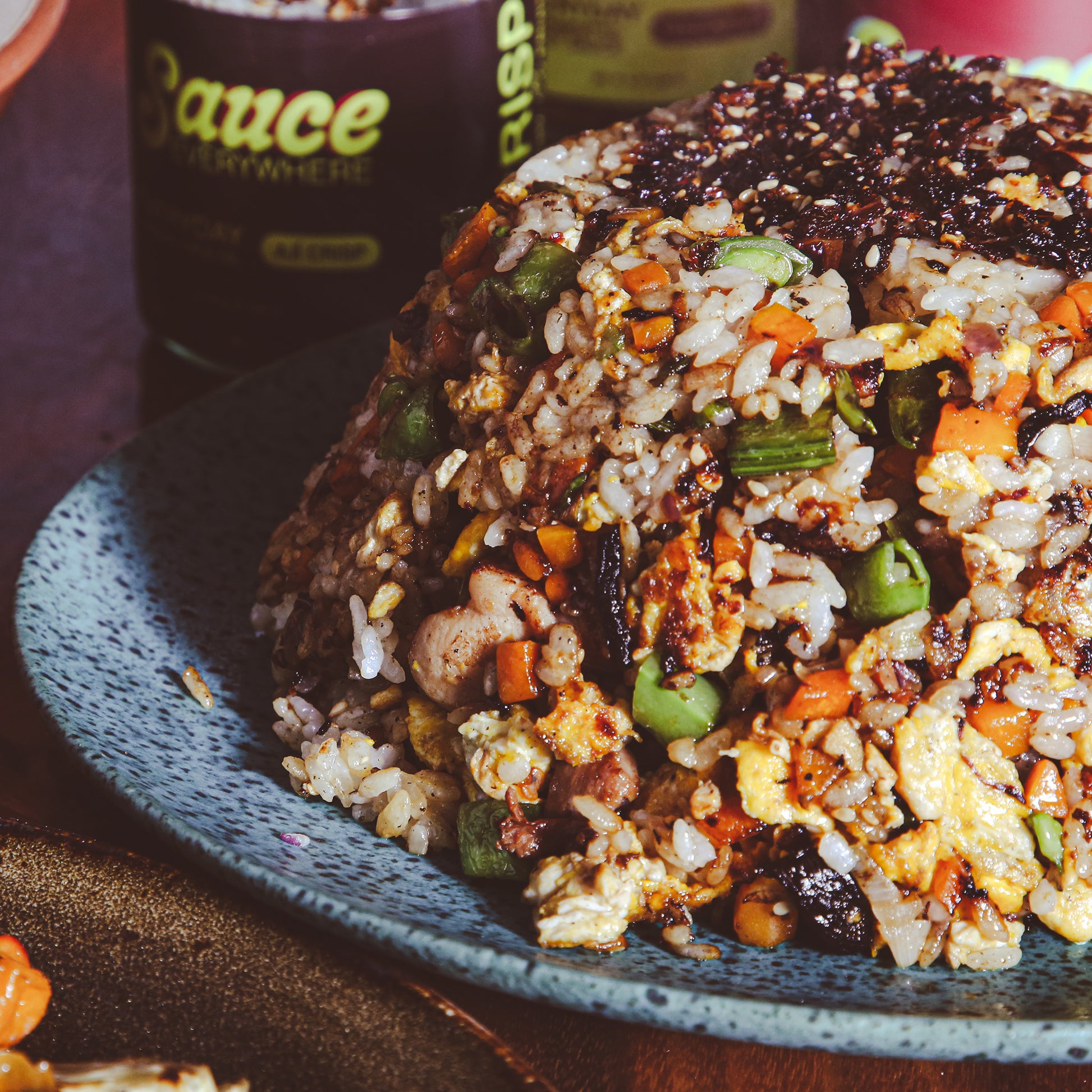 Mound of chicken fried rice with chile sauce on plate in front of sauce jar.