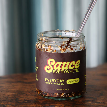 Close-up of open jar of chile sauce with spoon on wooden table.