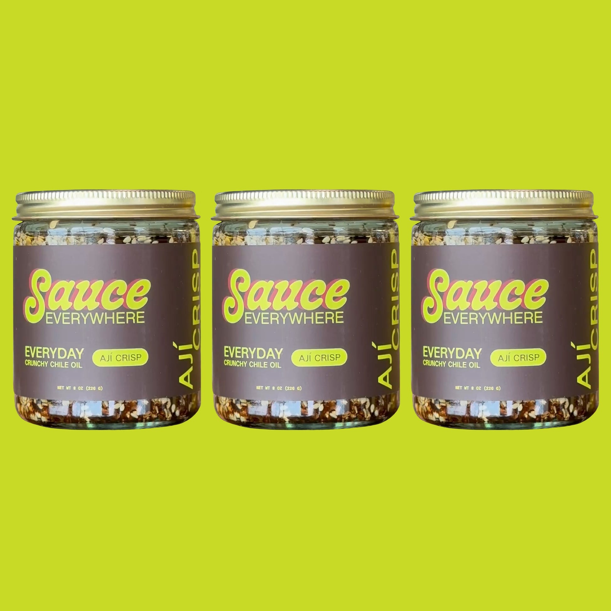 Three glass jars of Aji Crisp chile sauce by Sauce Everywhere against chartreuse background.