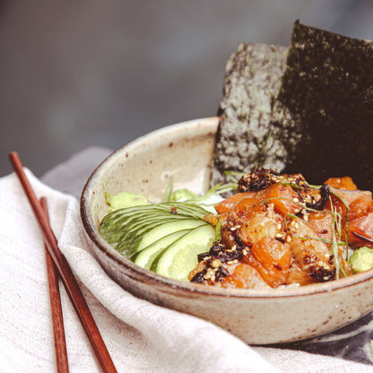 Raw trout and cucumber with chile sauce in bowl beside chopsticks and napkin.