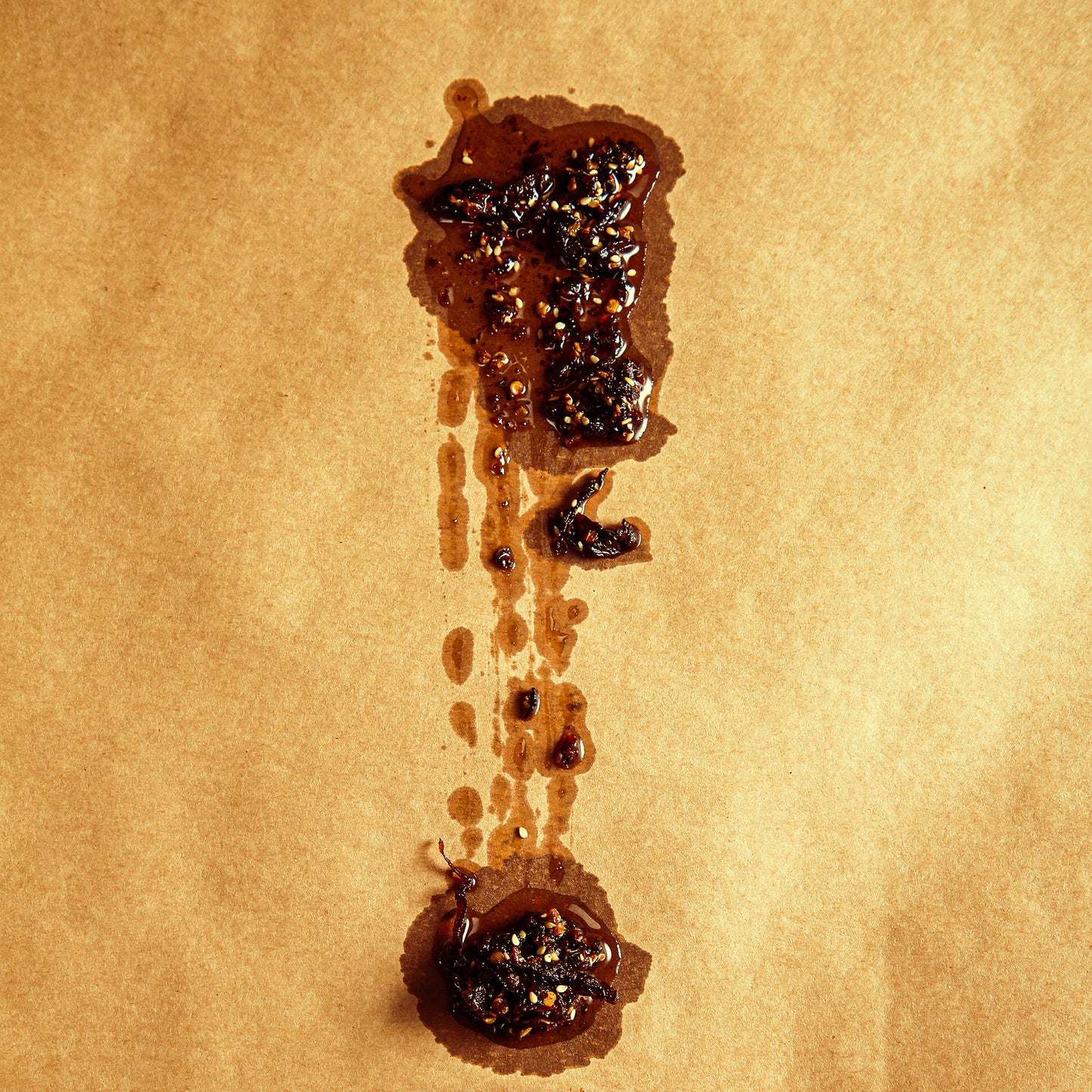 Dark brown Aji Crisp sauce with shallots and seeds smeared on butcher paper.