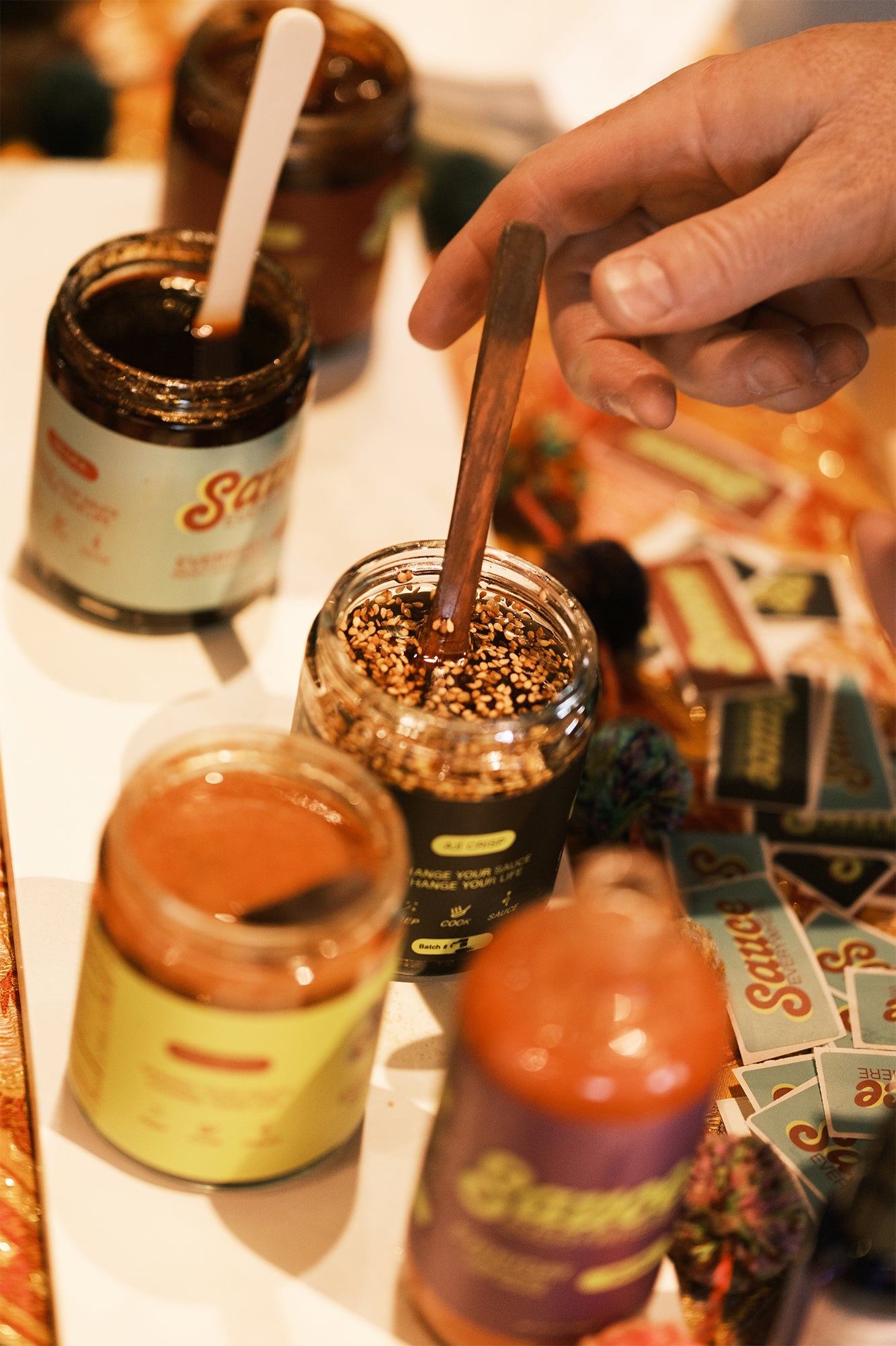 Open jars of chile sauces on table with hand reaching for serving spoon.