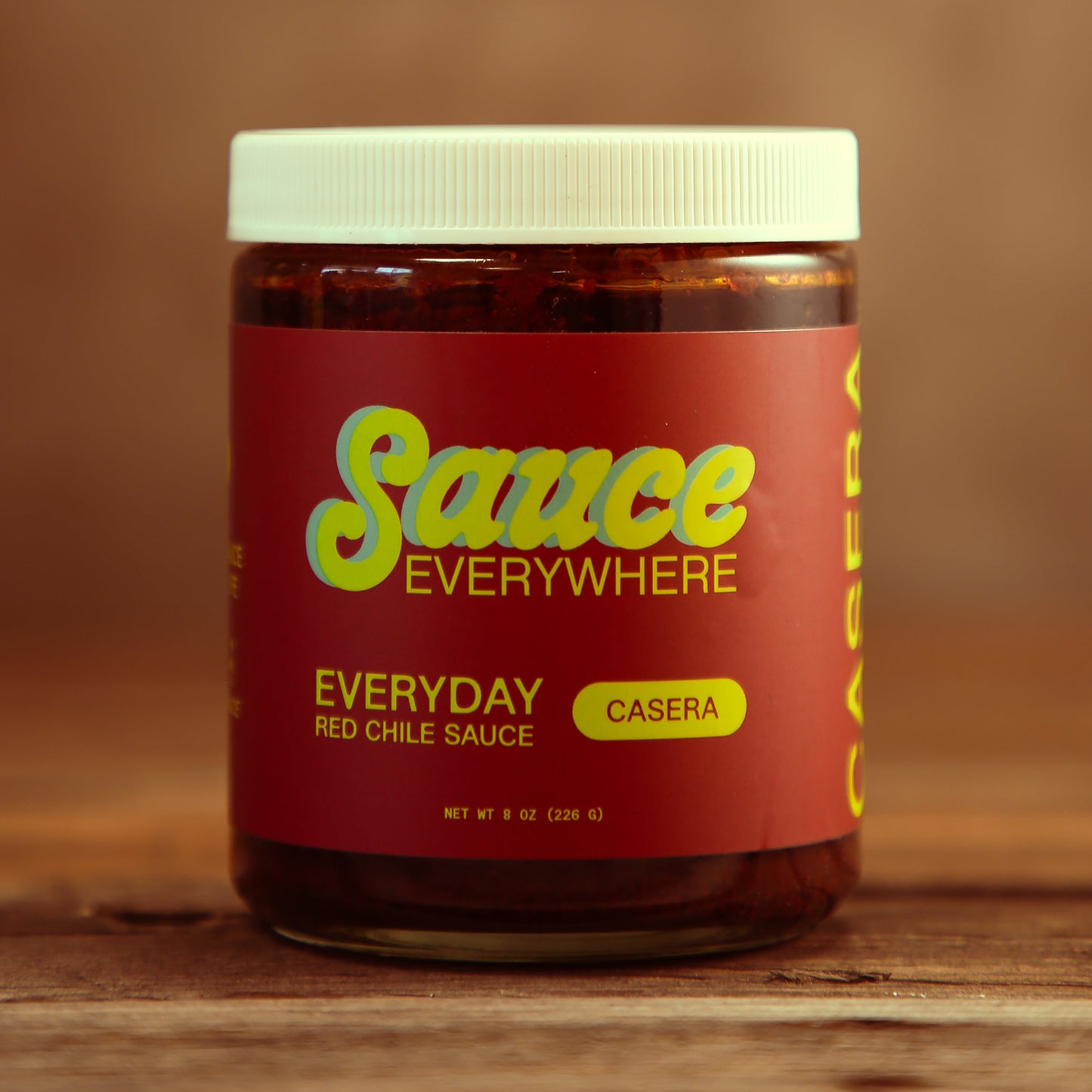 Unopened glass jar of Casera chile sauce by Sauce Everywhere on wooden table.