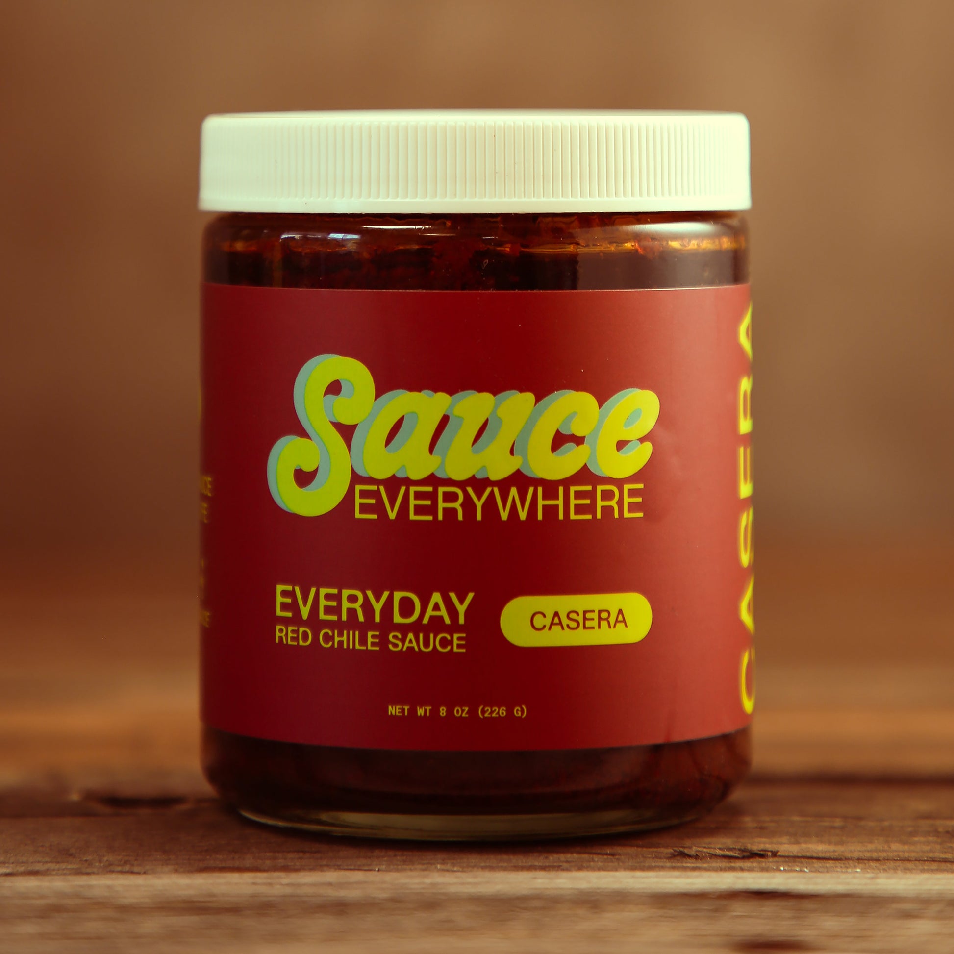 Unopened glass jar of Casera chile sauce by Sauce Everywhere on wooden table.