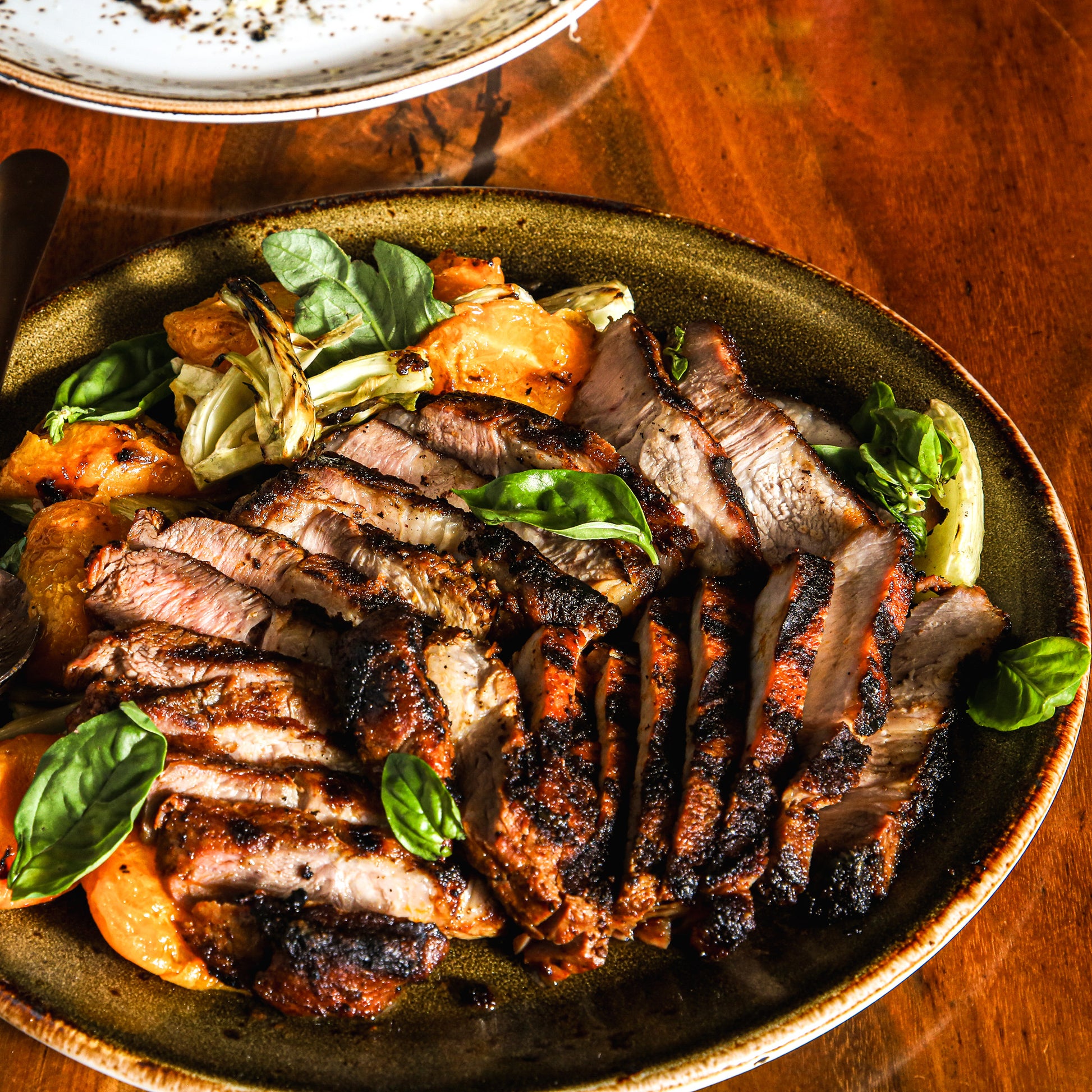 Slices of grilled pork with grilled apricots and basil leaves on serving plate.