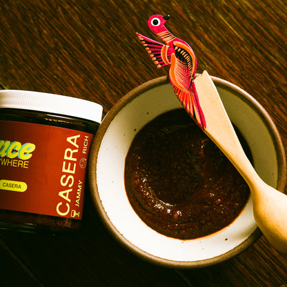 Casera sauce in side bowl with ornamental wooden spoon beside glass jar.