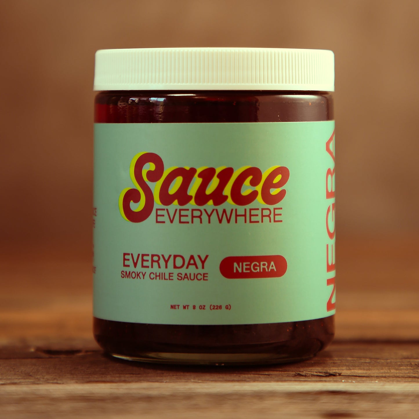 Unopened glass jar of Negra chile sauce by Sauce Everywhere on wooden table.