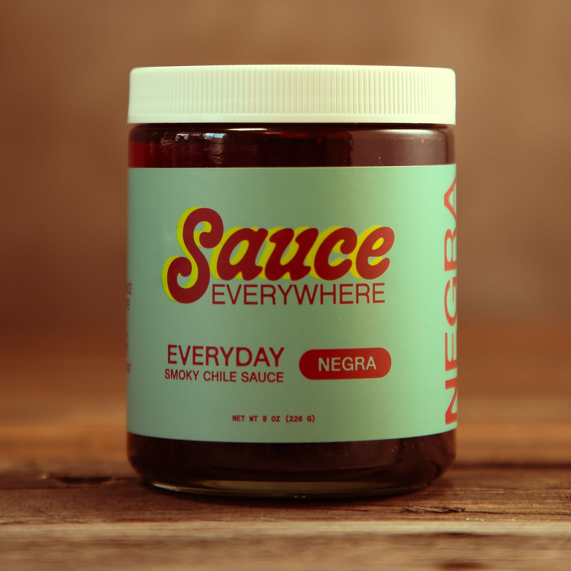 Unopened glass jar of Negra chile sauce by Sauce Everywhere on wooden table.