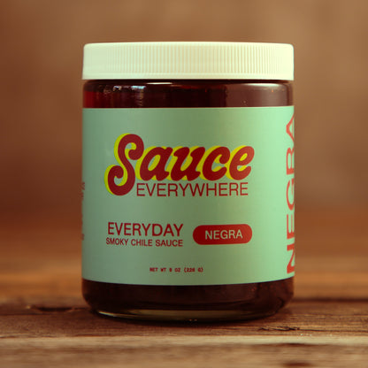 Unopened glass jar of Negra chile sauce by Sauce Everywhere on wooden table.