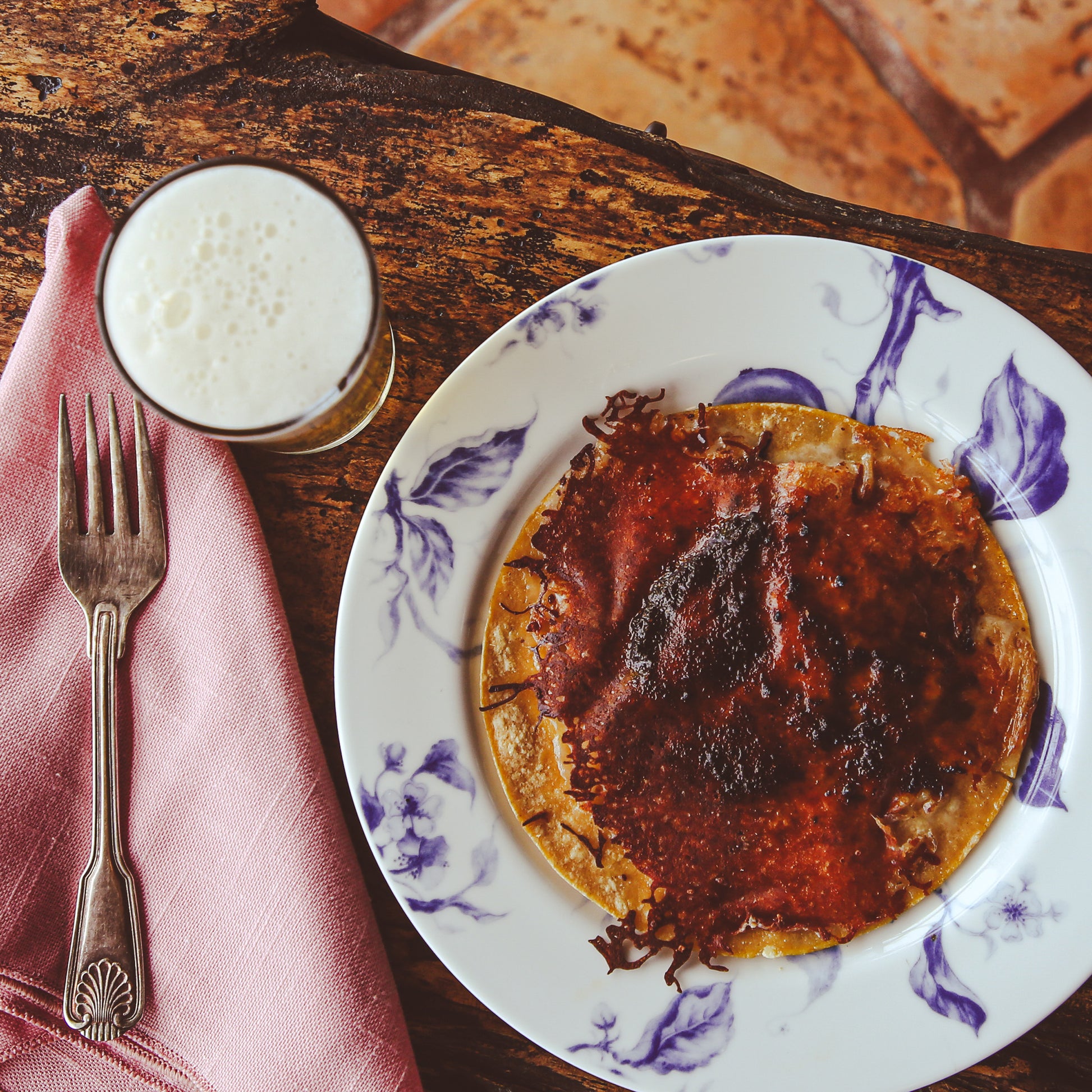 Quesadilla with chile sauce on dinner plate beside fork, napkin, and beverage.