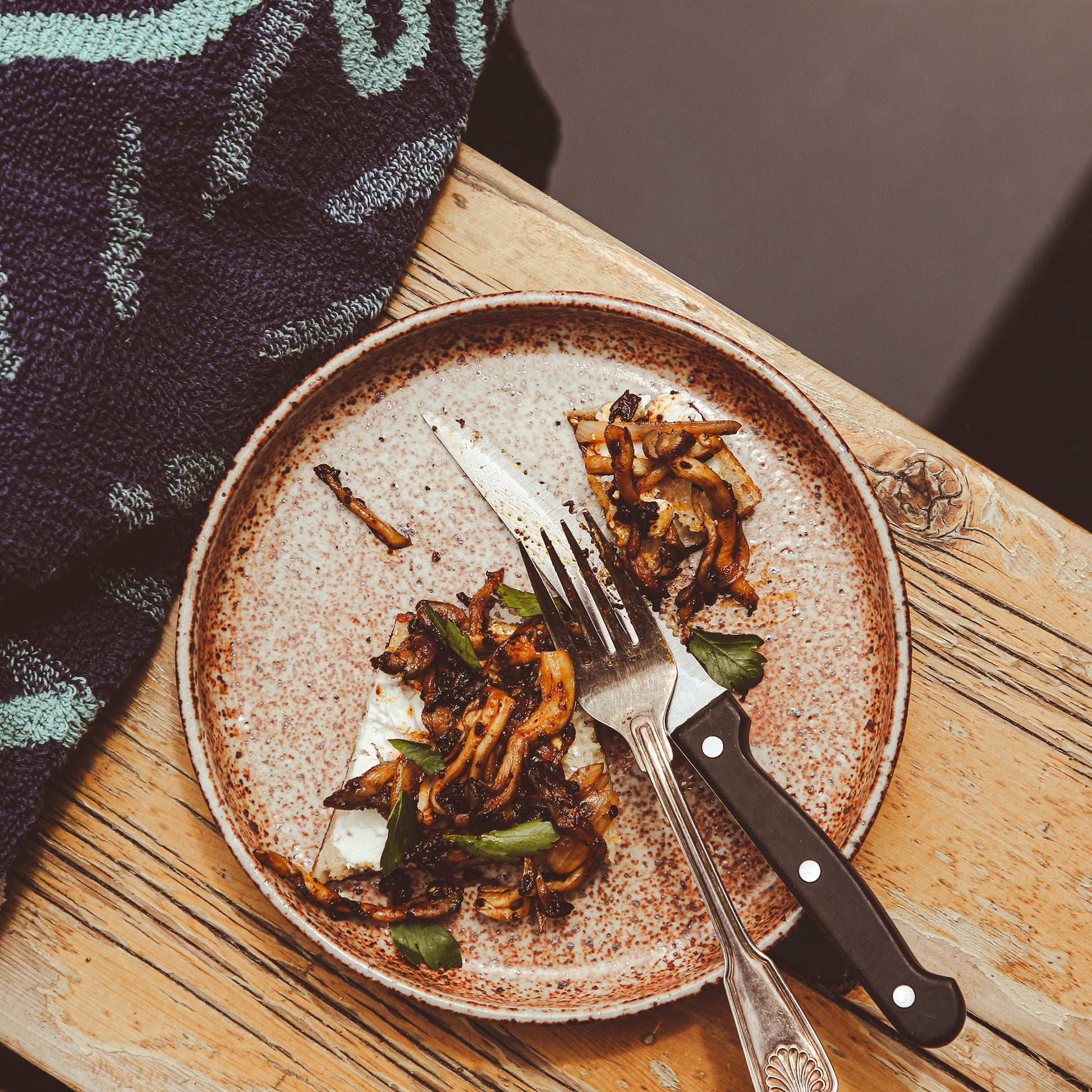 Knife, fork, and cut toast with marinated mushrooms on salad plate above pool.