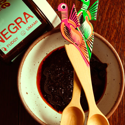 Negra sauce in side bowl with ornamental wooden spoons beside glass jar.