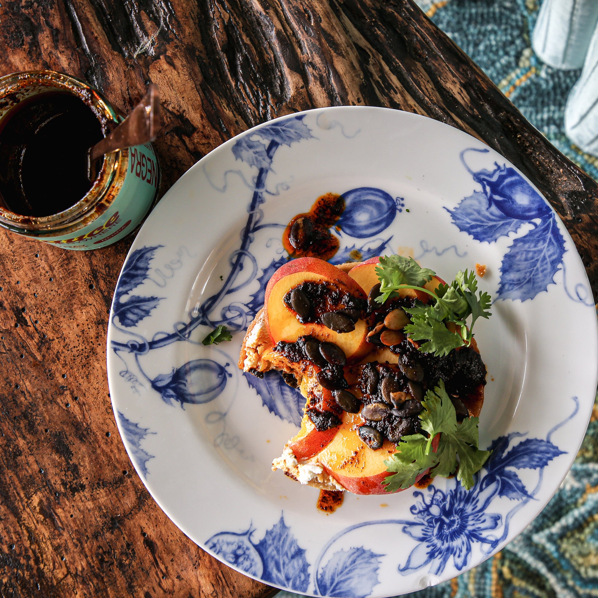 Close-up of tostada with peaches, toppings, and chile sauce on plate beside sauce jar.
