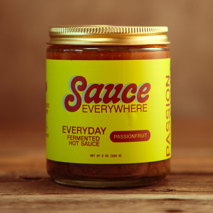 Unopened glass jar of Passionfruit chile sauce by Sauce Everywhere on wooden table.