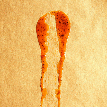 Red-orange Passionfruit sauce with black seed flecks smeared on butcher paper.