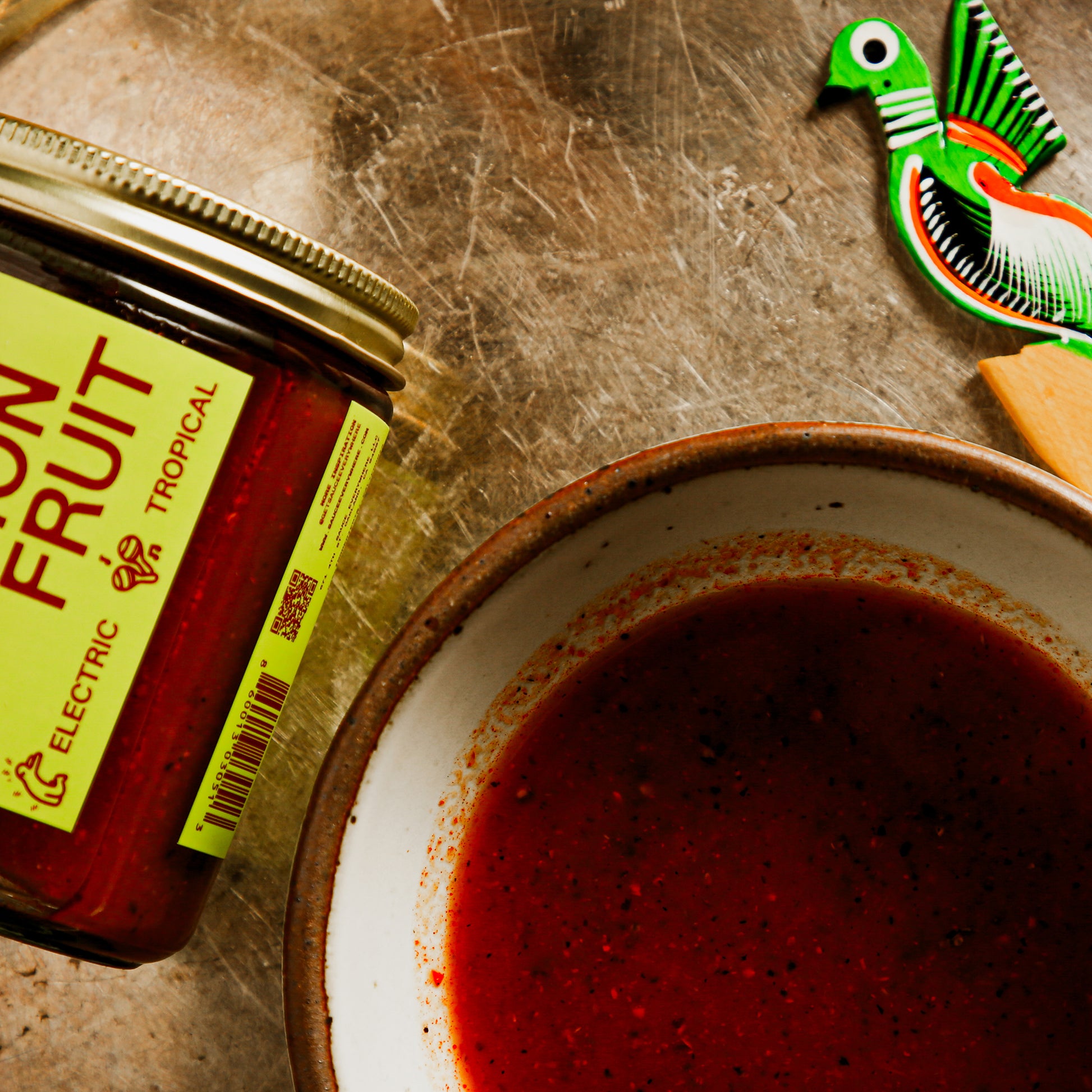 Passionfruit sauce in side bowl beside glass jar and ornamental wooden spoon.