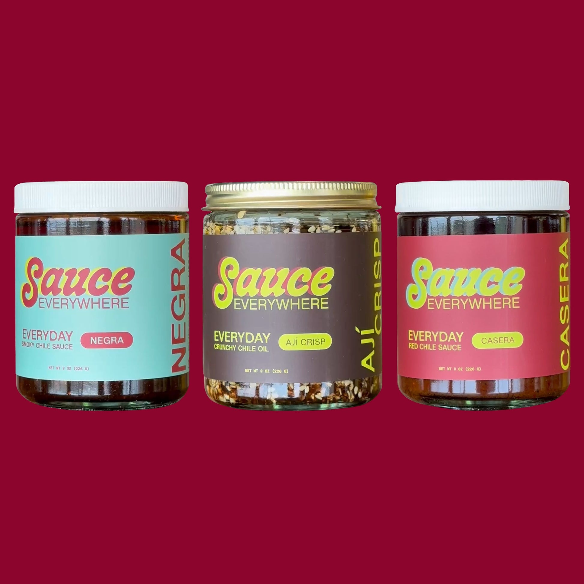 Three glass jars of chile sauces by Sauce Everywhere against maroon background.